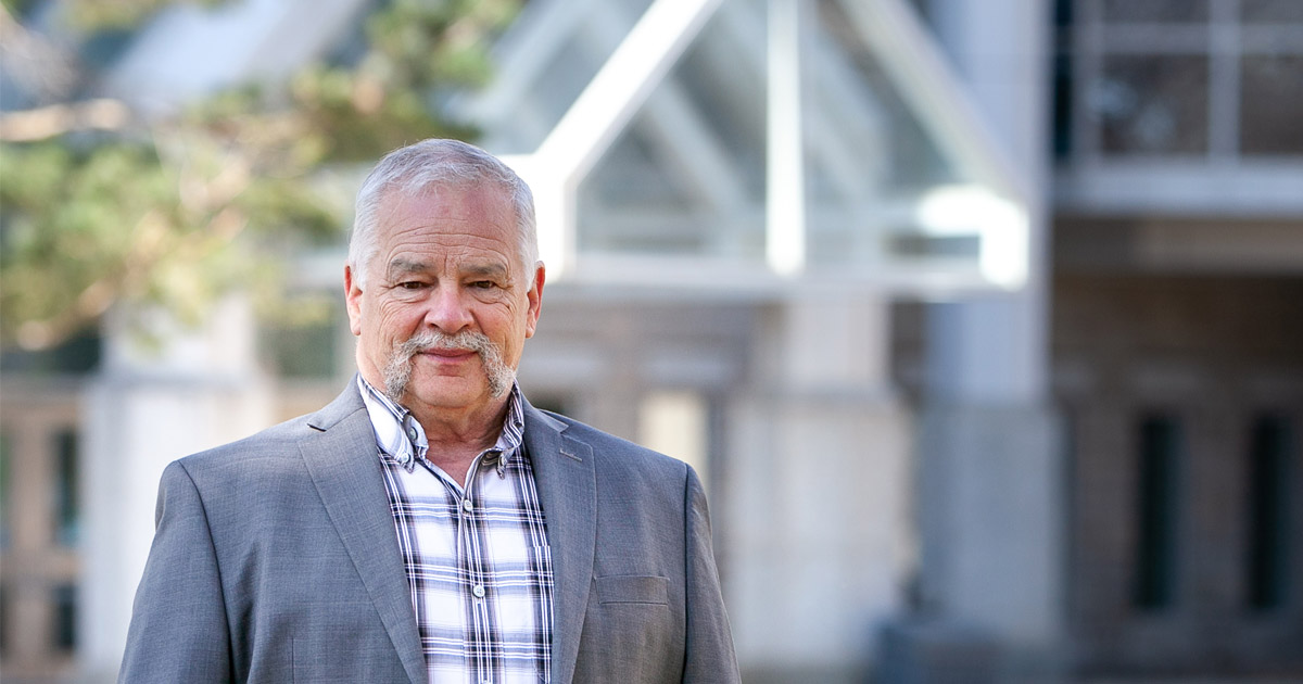Dr. Scott Wright, Director, Saskatchewan Agriculture, stands smiling in the sunshine with a coat and button up shirt.